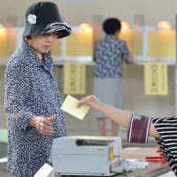 One ballot at a time: A woman receives her ballot for the Upper House election from an election board official at a polling station in Tokyo on Sunday. | AFP-JIJI