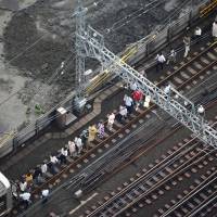 Single-file please: Passengers from a stranded train on the Tokyu Toyoko Line in Kawasaki are forced to get out and walk toward Motosumiyoshi Station after a thunderstorm caused a power outage Tuesday afternoon. | KYODO