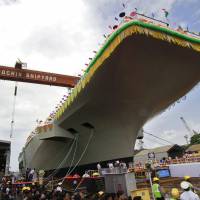Cochin Shipyard employees admire the INS Vikrant, India\'s first domestically built aircraft carrier, in the southwestern city of Kochi on Monday. The price tag for the 40,000-ton, 262-meter-long vessel, designed by the Indian Navy and constructed at the shipyard, is estimated at &#36;5 billion. | REUTERS/KYODO
