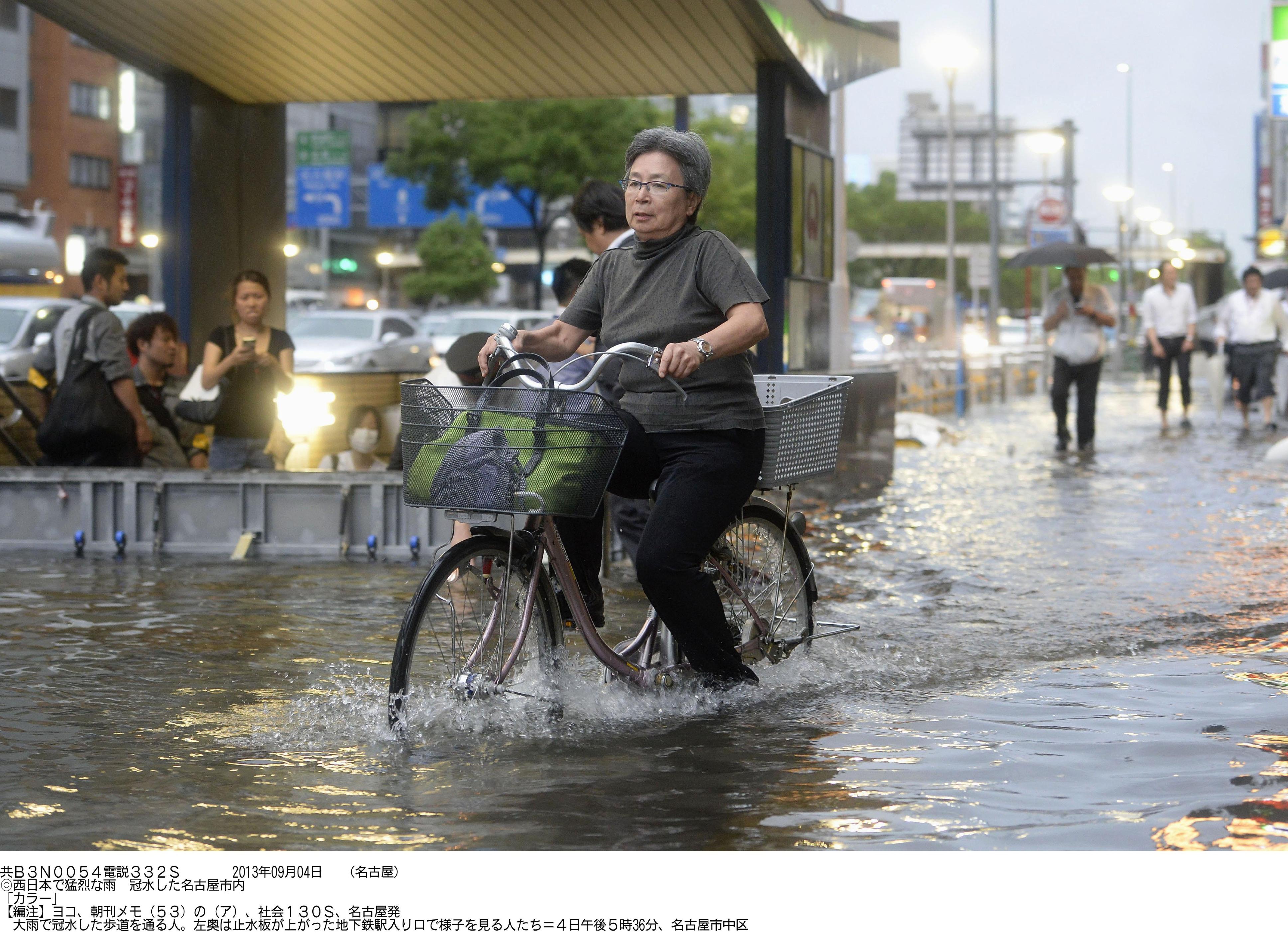 High and wet: A woman bicycles down a flooded street in Naka Ward, Nagoya, around 5:30 p.m. Wednesday as people look on from inside a subway station's flood barrier. | KYODO