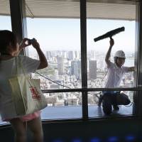 Something to see: A woman visiting the special observation deck at Tokyo Tower in Minato Ward photographs a window cleaner on Tuesday. A broken window on an elevator serving the deck, 250 meters above ground, forced a shutdown the same day. | AP