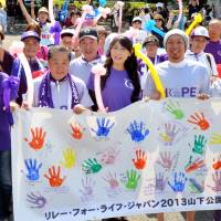 Cancer survivors, caregivers and supporters walk through Yamashita Park in Yokohama on Saturday as part of the Relay For Life, a charity event being held to raise public awareness about the disease. The participants will walk around the park for 24 hours straight until noon Sunday while holding a banner bearing handprints and messages from cancer survivors. | YOSHIAKI MIURA