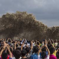People take pictures of massive waves caused by Typhoon Usagi in Hangzhou, Zhejiang province, China, on Sunday. The storm killed at least 25 people after crashing ashore in southern China and throwing the region\'s transport systems into chaos on Monday. \"Usagi\" is the Japanese word for rabbit.  | REUTERS/KYODO