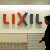 The fixture is in: An employee passes a sign for Lixil Group Corp. at their Tokyo offices on Sept. 26. | BLOOMBERG