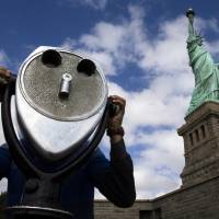 American icon: The Statue of Liberty looms over a visitor as he uses binoculars to look out over New York Harbor on Sunday. The statue was reopened to the public after New York state agreed to shoulder the costs of running the site during the partial federal government shutdown.   | AP