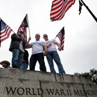 Battle lines drawn: Demonstrators watch from atop a wall as veterans accompanied by their families and supporters hold a rally Sunday at the World War II Memorial in Washington to protest its closure amid the U.S. government shutdown. | THE WASHINGTON POST
