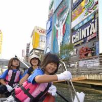 Shizune Nakanishi, 7, picks up garbage floating on the Dotonbori River in Osaka on Sunday. Riding in a rubber boat, she joined a two-day event to help clean up the river. A total of 150 people plan to participate through Monday. | KYODO