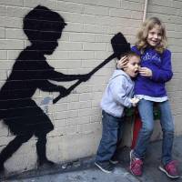Children pose Sunday in front of the silhouette of a boy swinging a sledgehammer toward a fire hydrant, painted by British graffiti artist Banksy. The mysterious street artist is 20 days into his monthlong project in New York. | REUTERS/KYODO