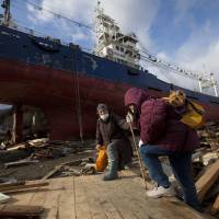 Survival tales: Two women pass by a ship that was washed into their neighborhood by the tsunami as they search for their destroyed home in the leveled city of Kesennuma, in northeastern Japan, March 17, 2011. | AP