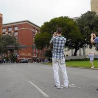 Cross road: Tourists stand in the middle of Dallas\' Elm Street last month to take pictures from the spot, marked by a X, where the fatal shot hit President John Kennedy in 1963. They are looking up at the Texas School Book Depository (left). The sixth-floor window where Lee Harvey Oswald fired his rifle is on the right, the second row from the top.  | THE WASHINGTON POST