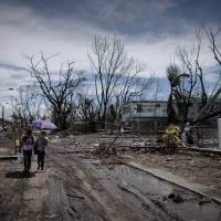 Desperation: Typhoon victims walk through land ravaged by Typhoon Haiyan in Tacloban, on the eastern island of Leyte, on Wednesday. Typhoon-struck Philippine city holds first mass burial