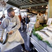 Natural taste: Scott Smith tosses a fresh salmon to a colleague behind the counter at the Pike Place Fish Market in Seattle in October 2010. Television ads featuring Pike Place fishmongers, organic farmers and others have hammered the proposal to label food produced with genetic engineering. Washington state to vote on mandatory GM labels