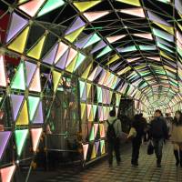 People tour an illuminated tunnel built as a lattice of triangular panels at the Tokyo Dome City amusement complex on Wednesday. The 80-meter-long artwork, set aglow by light-emitting diodes in various colors, is part of the site\'s annual illumination event, which will run until Feb. 16. | SATOKO KAWASAKI