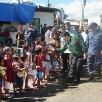 Reality check: Defense Minister Itsunori Onodera is greeted by children at an evacuation facility in the Philippine city of Tacloban, which was heavily damaged by Typhoon Haiyan. Onodera was on a two-day visit that started Saturday. | KYODO