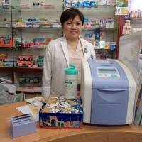 One of the store\'s pharmacists, Akiko Nagai, gives an explanation about the simple diabetes test while standing next to a device designed to measure glycated hemoglobin in blood. | MAMI MARUKO