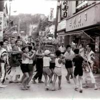 Youth movement: This photo taken on Aug. 22, 1964, shows children carrying a \"mikoshi\" float through Takeshita-dori during a summer festival. Seen in the background are the trees of Meiji Shrine. | COURTESY OF HARAJUKU TEKESHITA-DORI SHOTENGAI