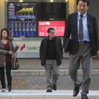Frothy again?: Pedestrians walk in front of a monitor displaying the closing figure of the Nikkei average outside a securities firm in Tokyo last month. | BLOOMBERG