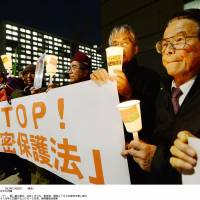Fighting the law: Demonstrators hold candles and signs at the Diet on Monday during a protest against the state secrets bill being deliberated in the Upper House. | KYODO
