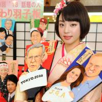 A worker shows off doll-maker Kyugetsu\'s \"hagoita\" ornamental paddles with newsmakers of 2013, including ex-IOC President Jacques Rogge and Britain\'s baby Prince George, in Taito Ward, Tokyo, on Thursday. | SATOKO KAWASAKI