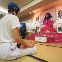 A follower meditates before portraits of Aum guru Shoko Asahara in Tokyo in August 1999. | AFP-JIJI