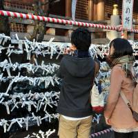 Visitors to Tokyo\'s Yushima Tenjin Shrine tie white paper ribbons bearing written fortunes on to wooden racks. The ribbons are called \"o-mikuji,\" which literally translates as \"sacred lottery.\" | YOSHIAKI MIURA