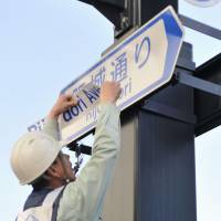 Foreigner-friendly direction: A worker covers a transliteration of a Japanese street name with its English equivalent on Wednesday in the city of Hiroshima. | KYODO