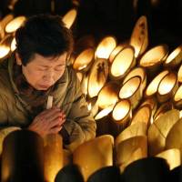 Prayers amid the lights: A woman prays for the victims of the 1995 Great Hanshin Earthquake early Friday at a park in Kobe\'s Chuo Ward, where bamboo lanterns were arranged to mark the 19th anniversary of the killer quake. | KYODO