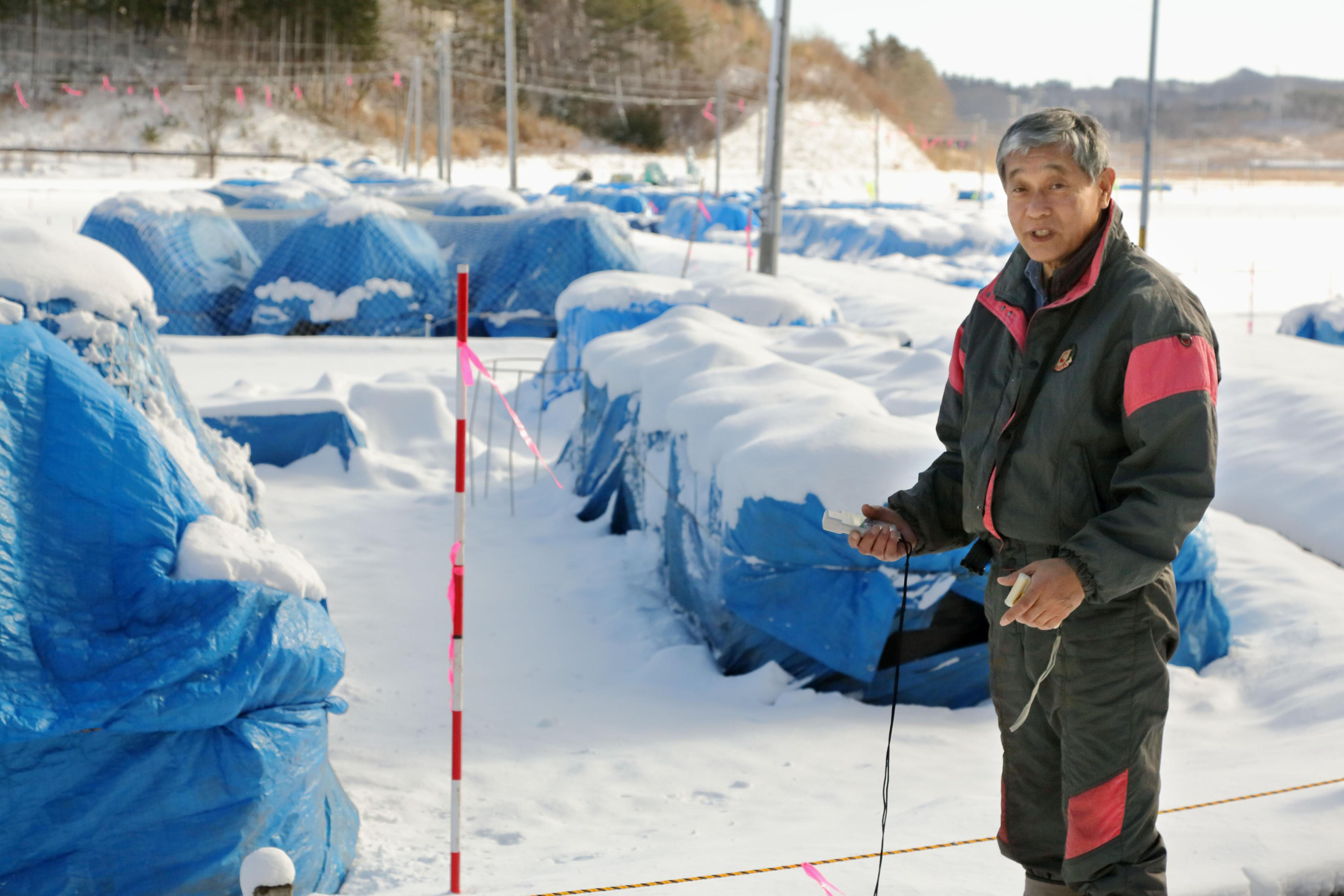 Victim of circumstance: Nobuyoshi Ito, who describes himself as an 'apprentice farmer,' holds a dosimeter in front of snow-covered bags containing contaminated dirt and sand in the village of Iitate, Fukushima Prefecture, on Dec. 15. | KYODO