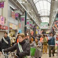 People lead bicycles through the Tenjinbashisuji shopping arcade Friday in Kita Ward, Osaka, to promote its cycling ban. Touted as Japan\'s longest shopping arcade, local shops pushed for the ban following several cycling accidents along the 2.6-km stretch of stores. About 35,000 people visit the arcade on its busiest days. | KYODO