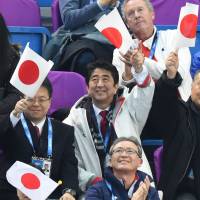 Prime Minister Shinzo Abe and former Prime Minister Yoshiro Mori (far right) wave the Japanese flag while attending the women\'s figure skating team short program on Feb. 15. | AFP-JIJI
