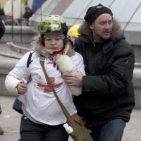 A woman is helped after being shot in her neck by a sniper bullet, in Kiev\'s Independence Square, the epicenter of the country\'s current unrest, on Thursday. | AP