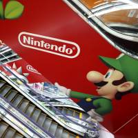 A customer rides past a Nintendo Co. advertisement on an escalator at an electronics retailer in Tokyo in April 2013. | BLOOMBERG