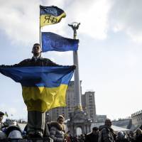 A man holds a Ukrainian flag as he stands in Independence Square, Kiev, on Monday after an arrest warrant was issued for ousted President Viktor Yanukovych for the \"mass murder\" of protesters. | AFP-JIJI