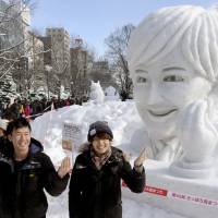 Visitors to the Sapporo Snow Festival mimic a snow sculpture of TV celebrity Christel Takigawa, who helped Tokyo win its 2020 Olympic bid last year with her \"omotenashi\" (the spirit of selfless hospitality) gesture. | KYODO