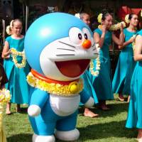 A Doraemon mascot is welcomed by hula dancers in Honolulu on Saturday, the opening day for an exhibition of drawings of the popular manga character at the Bernice Pauahi Bishop Museum. The exhibition runs through April 20. | KYODO