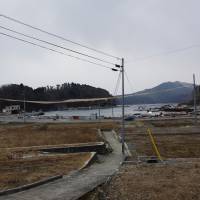 An orange banner is hung at the height of a 9.9-meter seawall that the Miyagi Prefectural Government plans to build to block possible tsunami at Kesennuma’s Shibitachi fishery port on Feb. 25. Many housing lots, destroyed by tsunami three years ago, are still empty. | REIJI YOSHIDA