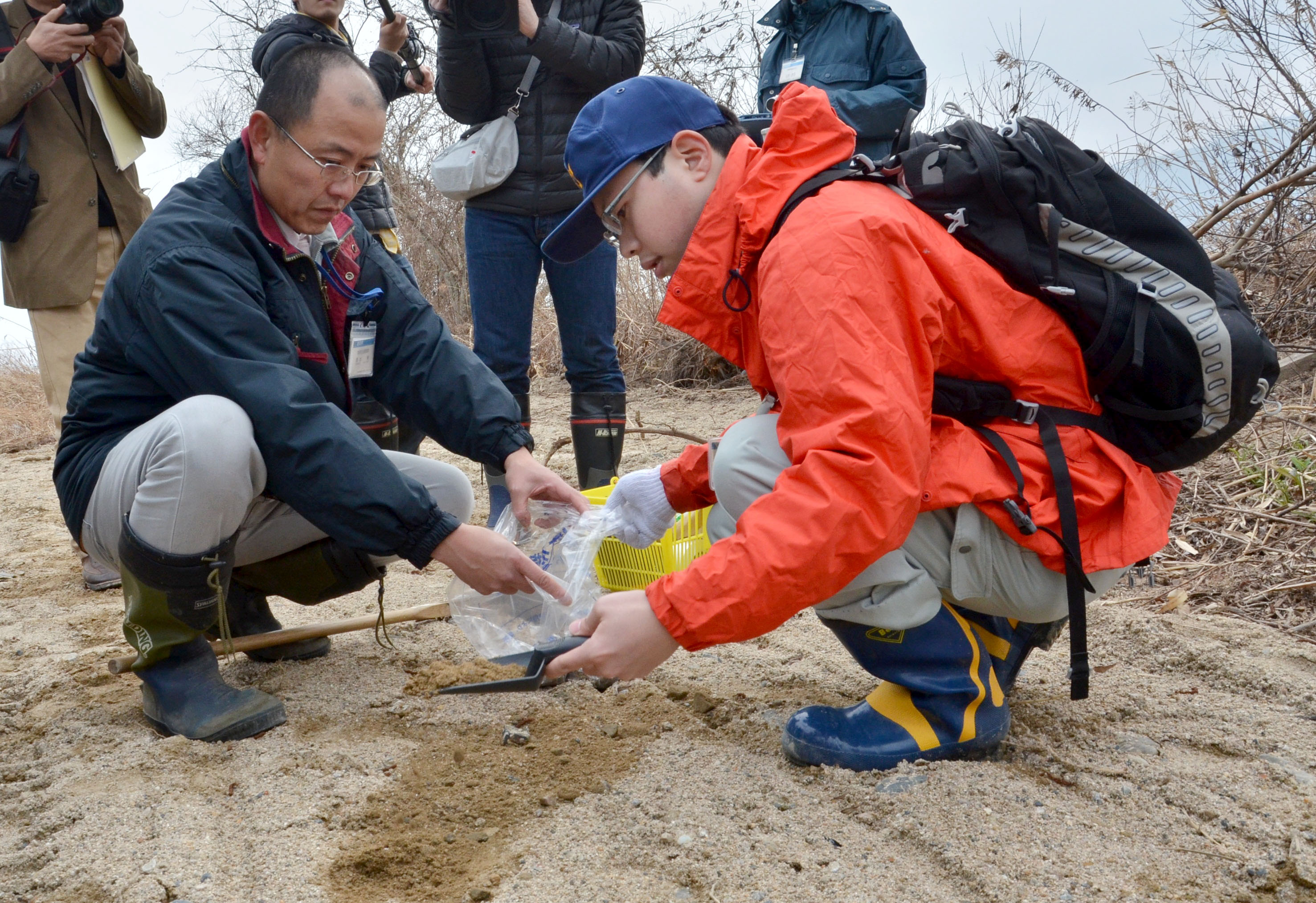 Shiga prefectural officials collect soil samples near a riverbank in Takashima on Feb. 28. Dozens of bags of cesium-contaminated wooden chips were found dumped there last year. | KYODO