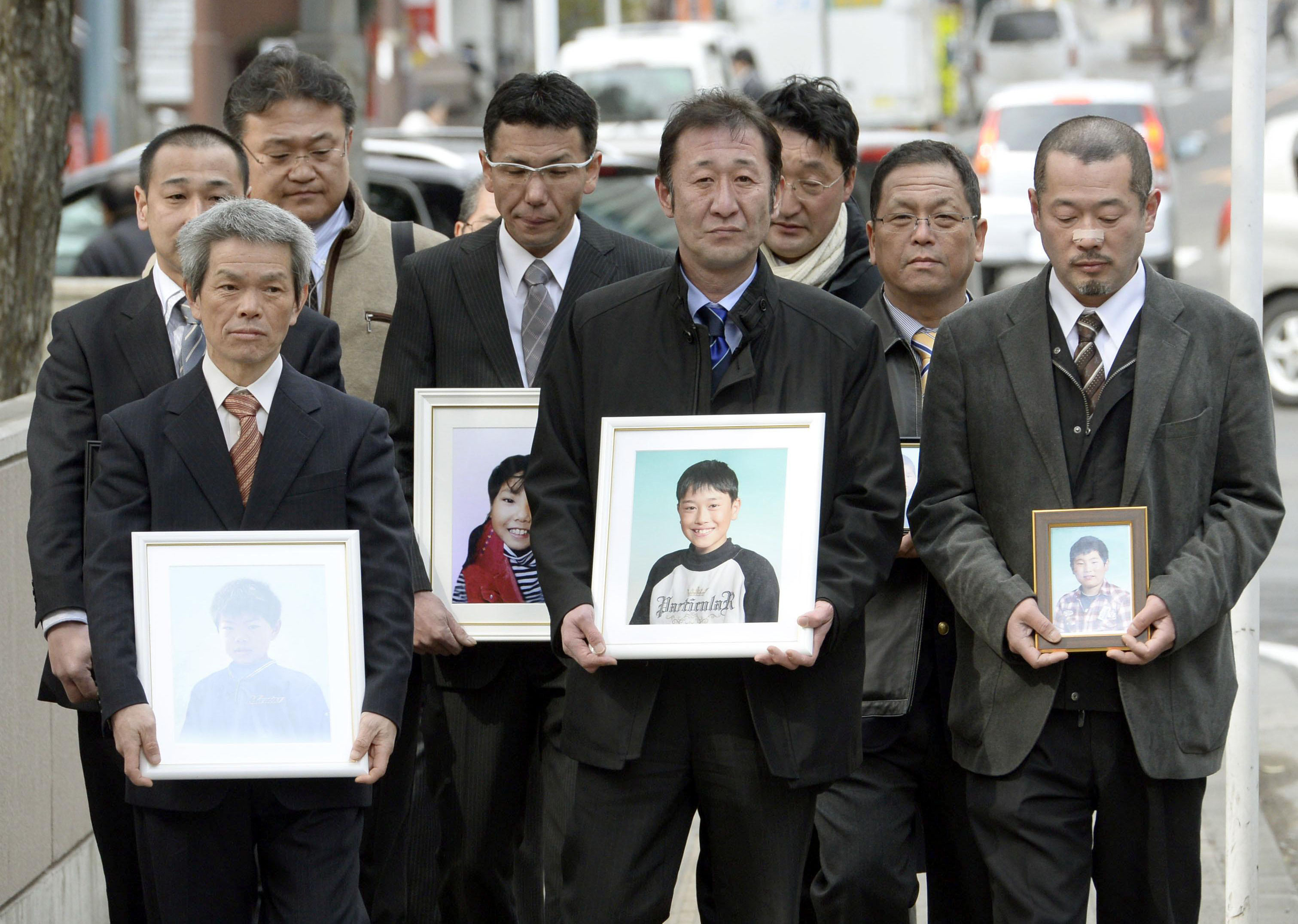 Relatives of Okawa Elementary School students killed in the March 2011 tsunami enter the Sendai District Court on Monday, holding the victims' photos. | KYODO