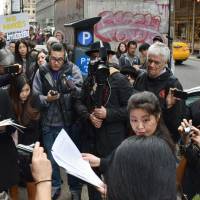 Anti-nuclear activists stage a protest surrounded by members of the media Tuesday in front of the Japanese Consulate General in New York. | KYODO