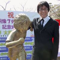 Yoichi Takahashi, creator of the popular manga and anime series \"Captain Tsubasa,\" pats the back of a newly installed bronze statue of Taro Misaki, one of the series\' main characters, in Katsushika Ward, Tokyo, on Sunday. | KYODO
