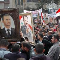 Demonstrators hold up pictures of Syrian President Bashar Assad and their national flag during a pro-government rally in Damascus on March 3. | AFP-JIJI
