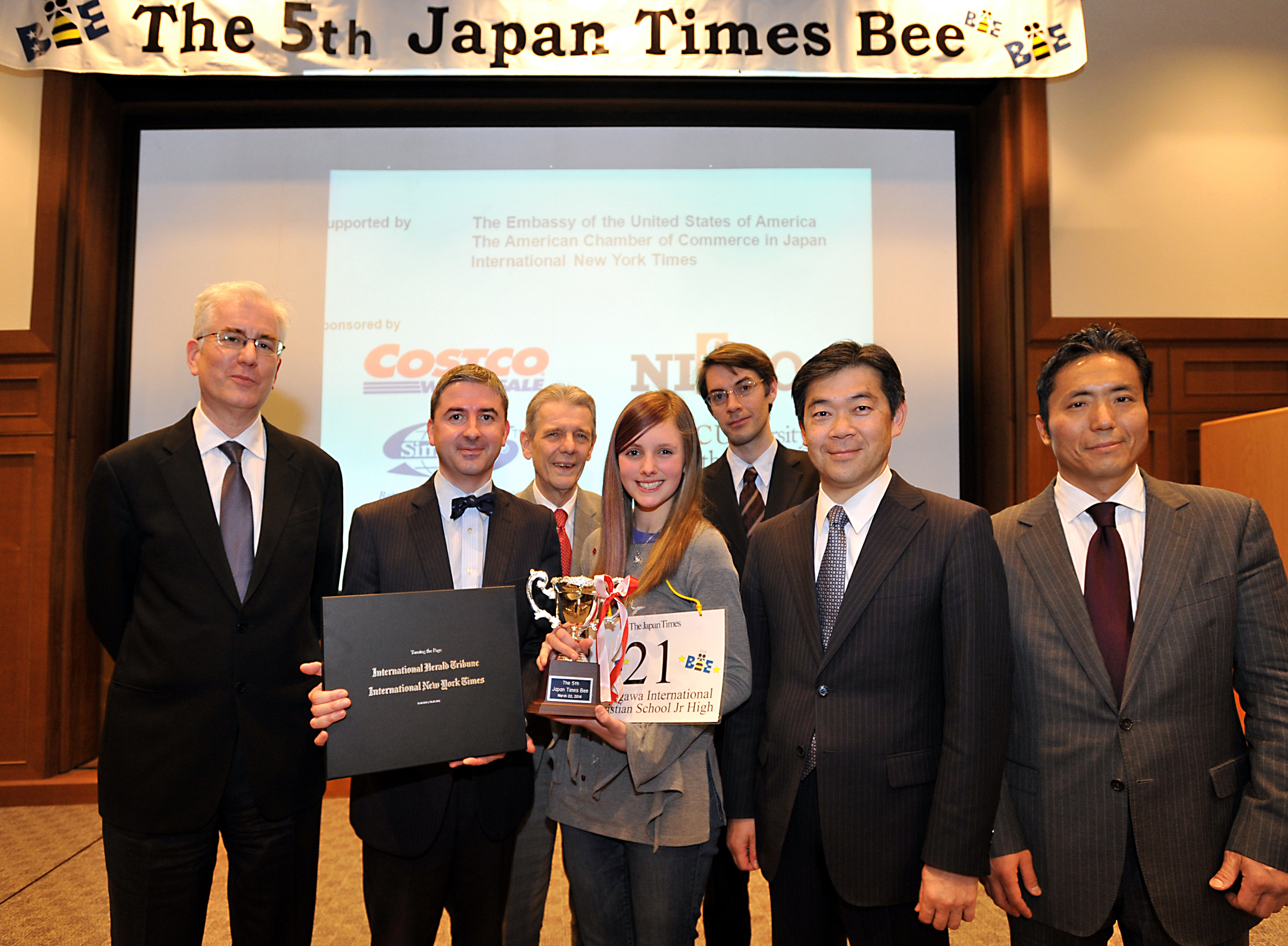 Michaella Bostrom stands with (from left) spelling judge Steve McClure, master of ceremonies Marc Davies, pronouncer James Tschudy, Japan Times Deputy Managing Editor Edan Corkill, Japan Times President Takeharu Tsutsumi and Shigeo Yushita, commercial director and head of Japan for the International New York Times. | YOSHIAKI MIURA