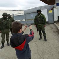 A boy photographs military personnel, believed to be Russian servicemen, standing outside a Ukrainian military unit\'s base outside Simferopol on Tuesday.  | REUTERS