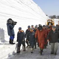 Workers walk on the snow-cleared Hakkoda Towada Goldline highway in Aomori Prefecture during a ceremony Thursday to commemorate the completion of snow-removal work. Cars will be allowed to resume travel on the scenic road on Tuesday. | KYODO