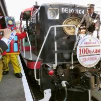 A railway employee poses for a photo with a young boy who was the millionth passenger on the Arashiyama Trolley, during a celebration Wednesday at Torokko Sagano Station in the city of Kyoto. The retro trolley began service in 1991 on a 7.3-km stretch of track between the station and the city of Kameoka in an area that has become a major tourist spots. | KYODO