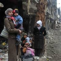 This photo, released by Syrian news agency SANA, shows residents of the besieged Yarmouk Palestinian refugee camp on the southern edge of Damascus waiting to leave on Feb. 4. | AP
