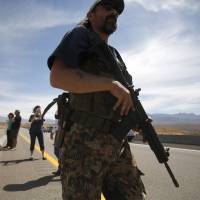 A protester carries a rifle on a bridge next to the Bureau of Land Management\'s base camp in Bunkerville, Nevada, on April 12. | REUTERS