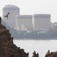 A man dives into the sea as Kansai Electric Power Co.\'s Mihama nuclear power plant looms in the background in the town of Mihama, Fukui Prefecture, in July 2011. | REUTERS