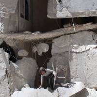 A Syrian girl on Monday collects her belongings from among the rubble of a building in the northern city of Aleppo after it was reportedly destroyed during an airstrike by government forces. | AFP-JIJI