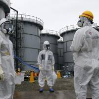 A Tokyo Electric Power Co. official (center) and journalists wearing protective suits and masks are seen standing near the H4 tank at Fukushima No. 1 nuclear power plant in Okuma, Fukushima Prefecture, last November. Radioactive water leaked from a storage tank in August. | AP